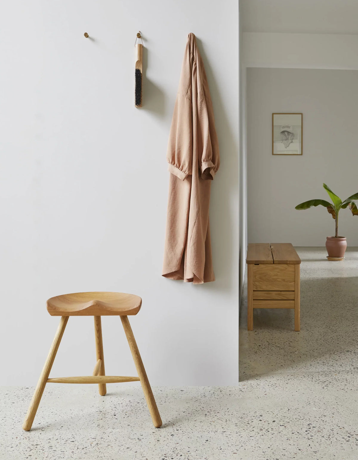 The Shoemaker Chair™ no. 49 in oak in a hallway, a coat on a peg rail and an A Line storage bench on terrazzo beyond — Courtesy Form & Refine