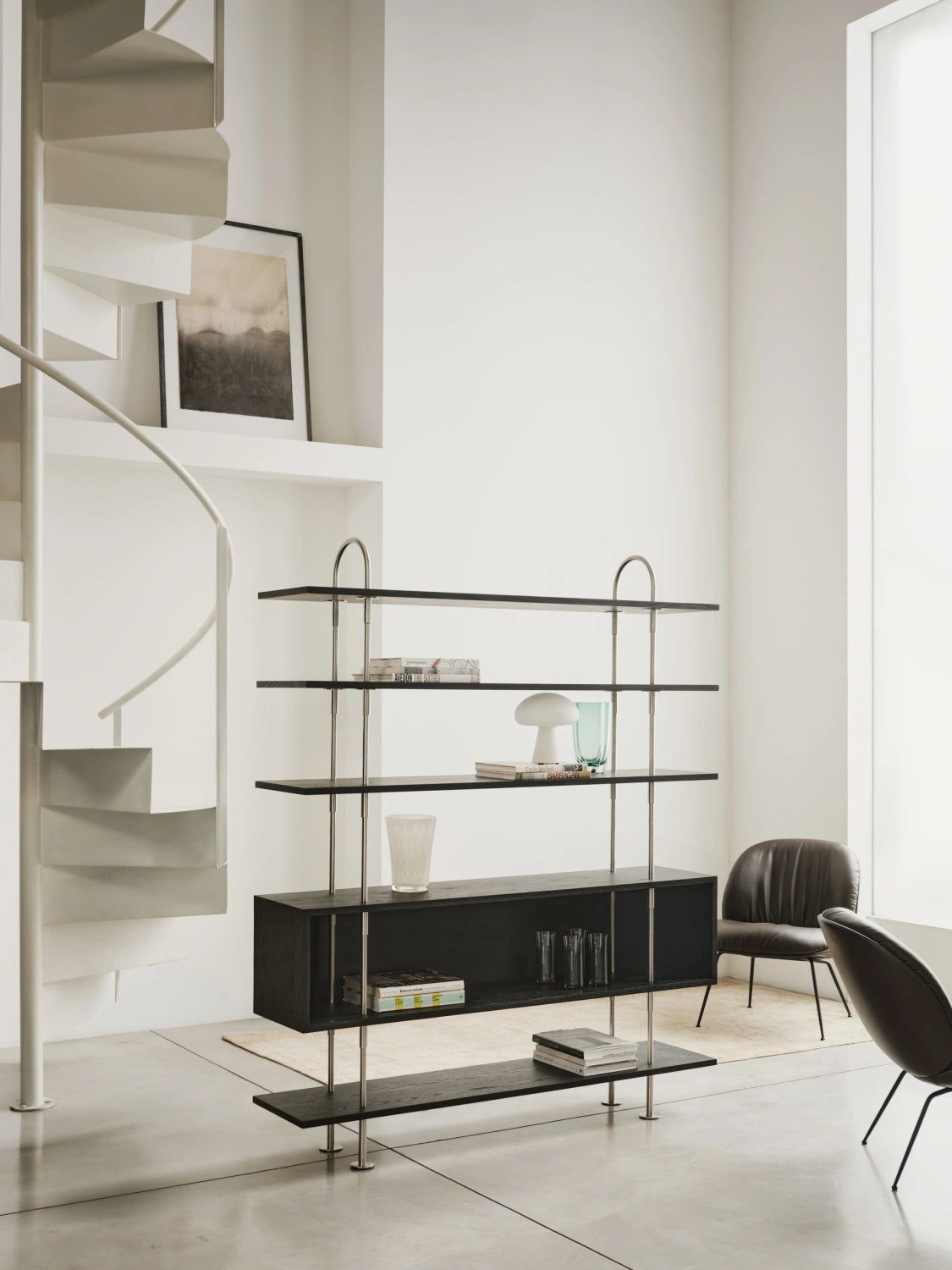 Tall GUBI Keen Shelving System with box shelf in a bright interior beside a spiral stair