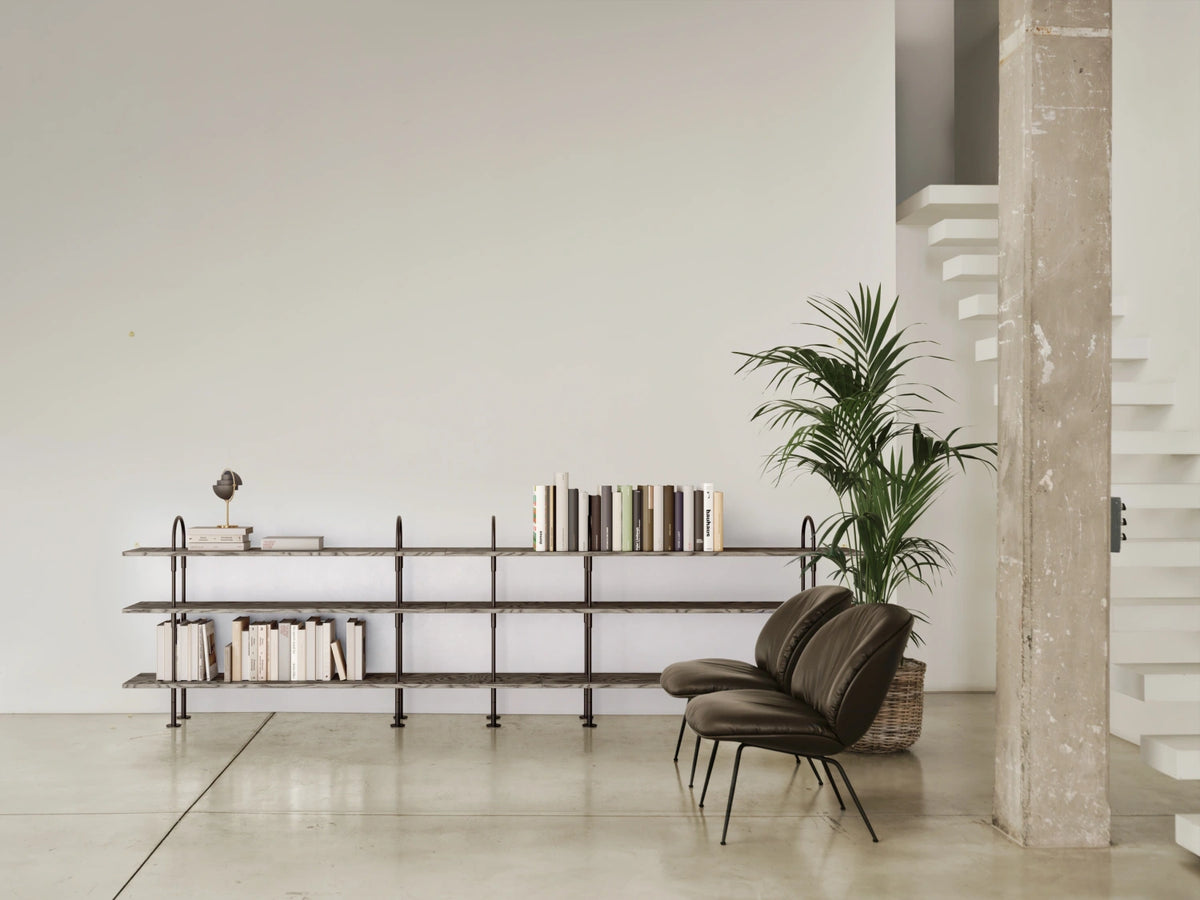GUBI Keen Shelving System in black brass and ALPI veneer across a pale living room wall